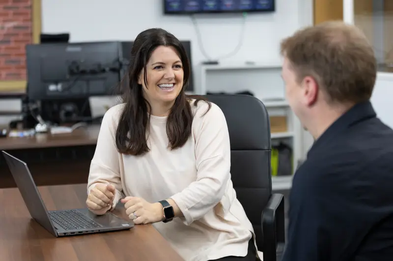 A CAP Technologies team member smiling as she talks with a colleague at her desk